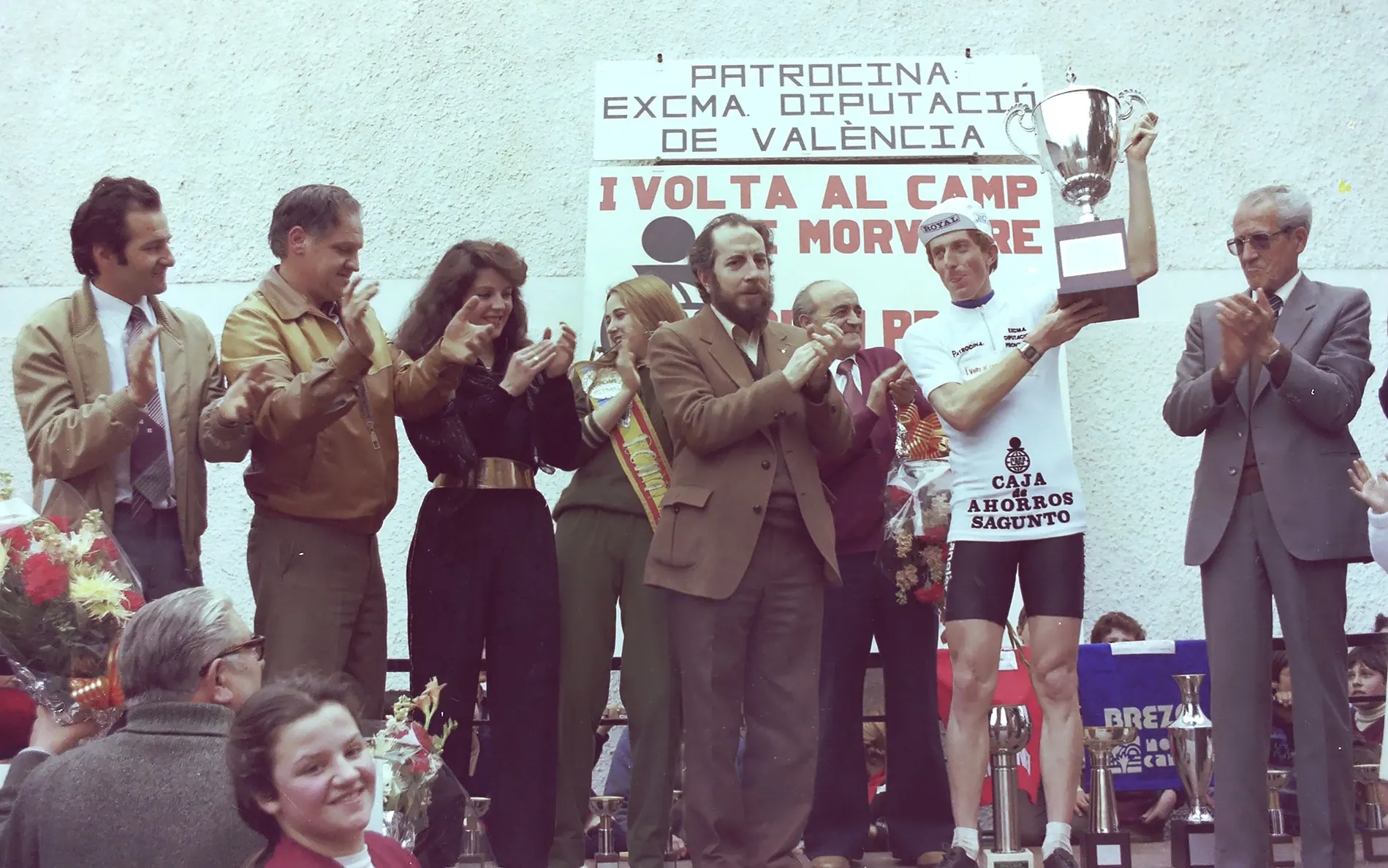 Gottfried Schmutz levanta la copa de vencedor en el podio de la I Volta al Camp de Morvedre, en 1982, bajo el cartel del patrocinio de la Diputación de València